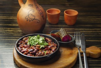 Lobio, dish in Georgian cuisine and salted cucumbers from beans and clay jug and cups on the table