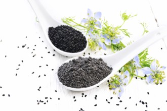 Flour and seeds of Nigella sativa in two spoons, sprigs of kalingini with blue flowers and green