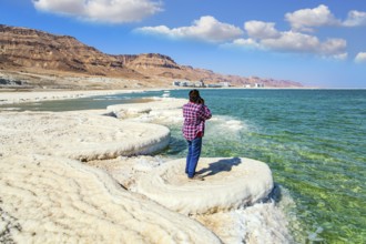 Woman in a plaid cowboy shirt photographs the sea surface. Evaporated salt forms beautiful crystals
