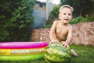 Toddler cute Caucasian white European race boy sitting hugging holding huge watermelon and smiling