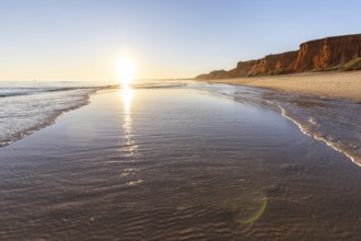 A landscape on the beach at low tide. The surrounding rocks and cliffs are reflected in the sea at