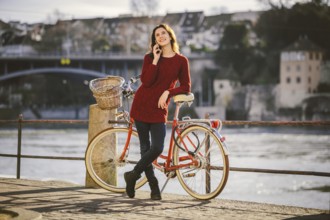 A young female traveler enjoying stands next to a bicycle near a river in the city of Basel.