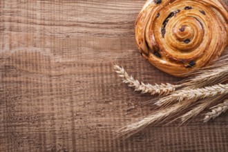 Sweet raisin bun bunch of wheat ears on oak wooden board food and drink concept