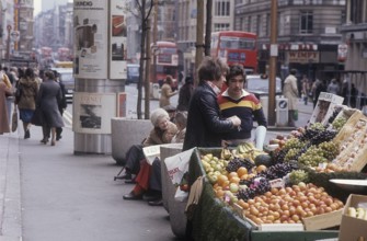 London 1982. A street view of a London street with a stand filled with fruit for sale. Credit