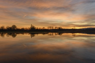 Trees reflecting in the water at sunset. Winter landscape red and orange sky. Bas-Rhin, Alsace,