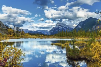 Lush cumulus clouds are reflected in the smooth water of the lake. Warm autumn day on the lake