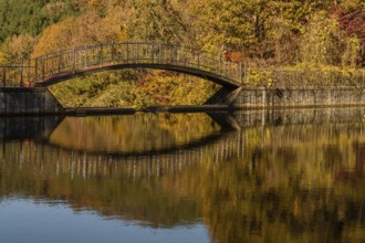 Footbridge over small pond in mountain valley with trees in beautiful fall colors in background,
