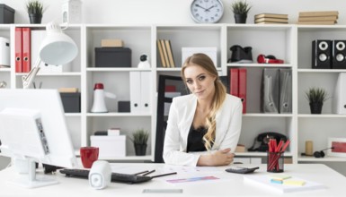 Beautiful young girl with blond hair in a white jacket and black blouse is working in the office.
