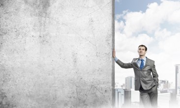 Handsome businessman leaning on cement blank wall. Place for text