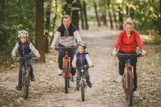 Parents and kids cycling on forest trail. family in warm clothes cycling autumn park. Family