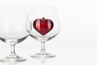 Red heart inside a glass of cognac on a glass plate