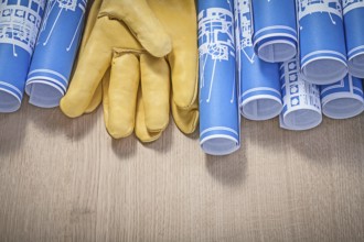 Blue rolled up construction plans leather protective gloves on wood board