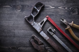 Obsolete vintage handsaw wire-cutter pliers on wooden board construction concept