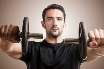 Personal Trainer doing front dumbell raises for training his deltoids in a brown background
