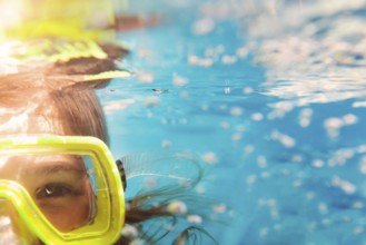 Little girl in colorful swimming mask smiling looking at camera under water