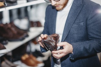 A man inspects a brown leather shoe on a store shelf