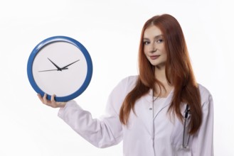 A female healthcare worker in a lab coat holding a clock, symbolizing time management in healthcare