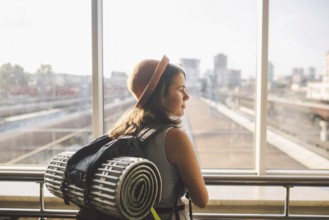Traveler Rear view woman standing at the window in hall Train Station departure with backpack,