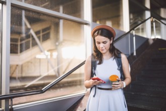Enjoy travelling. Female waiting train on station with backpack, using smart phone. Tourist makes
