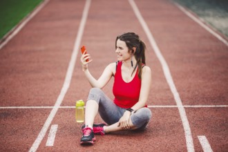 Young woman athlete at the stadium sporting lifestyle, sitting on the track, taking selfie photo on