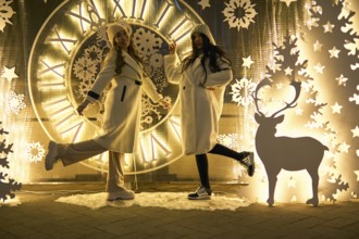 Two girlfriends asian girls in white coats are having fun hugging, new year, light bulbs