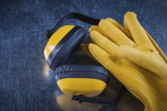 Safety yellow earmuffs and leather construction gloves on scratched metallic surface building