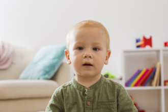 Portrait of a baby boy who is enchanted looks at the camera. The blond boy is sitting in the middle