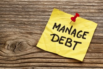 Manage debt - yellow reminder note against grained wood board