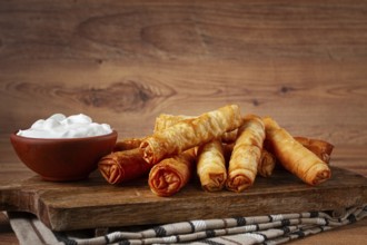 Fried spring rolls with cheese, on a wooden chopping board, with cream sauce, no people