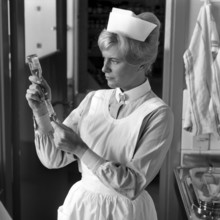 Nurse in the 1960s. A woman in a nurse uniform is preparing an injection and sucks the liquid from