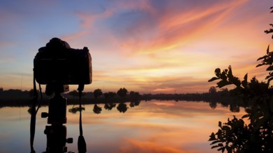 Silhouette of a camera at sunset.Dslr camera shooting on a cityscape sunset with lake reflection