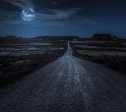 Moon, stars and clouds in the night. Wild west road illuminated from the moon. Moonlight and road