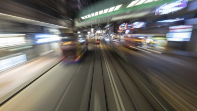 Tarveling through night Hong Kong by double-decker tram. View to road with moving bud and rails