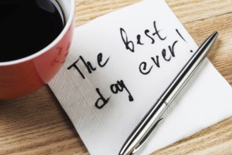 Coffee cup pen and napkin with words on wooden table