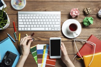 Web designer choosing colors from swatches at wooden desk. Top view office workplace with computer