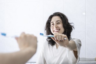 Portrait of a pretty young latin girl holding a toothbrush and smiling in front of the mirror.