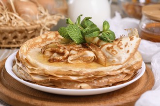 Homemade thin crepe (pancakes) with honey stacked in a stack, on a table with milk and eggs in a