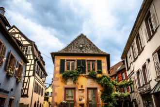 Characteristic half-timbered house with colourful shutters and floral decorations under a cloudy