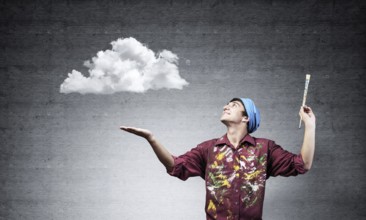Young artist drawing realistic white cloud. Male painter in dirty shirt and bandana with paintbrush
