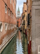 Narrow Venetian canal flanked by historic buildings with the bell tower in the distance. Venice,
