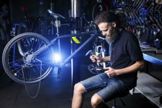 Young stylish bearded, with long hair Caucasian male mechanic worker at a bicycle workshop uses a