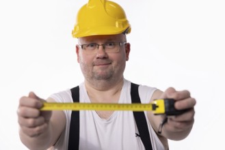 A construction worker in a yellow hard hat measures using a tape measure, showcasing tools of the