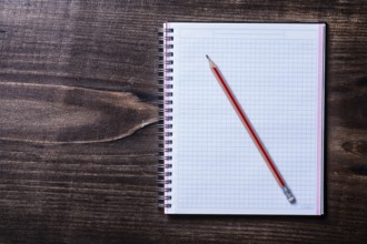 Pencil and checked copybook on wooden board education concept