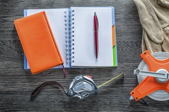 Rolled tape measures safety gloves notebooks pen on wooden board
