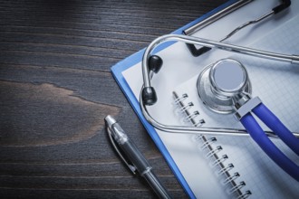 Clip board squared notepad pen and medical stethoscope tablet on vintage wooden background medicine