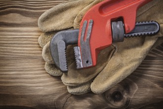 Pair of leather protective gloves pipe wrench on wooden board construction concept