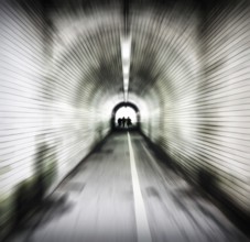 Zoom blur image of an old dark pedestrian tunnel with unidentifiable people emerging into the light