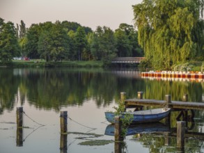 A quiet lake with boats and a jetty, surrounded by green nature at dusk, Pröbstingsee, Borken,