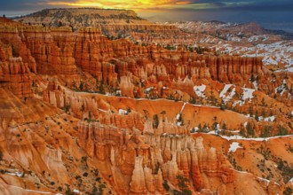 Wide view of a canyon with orange-coloured rocks and snow-covered slopes at sunrise, Bryce Canyon,