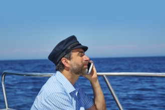 Captain cap sailor man talking mobile phone in boat sailng in the ocean sea